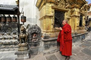 A Buddhist monk in red robes prays at a golden temple adorned with intricate carvings.